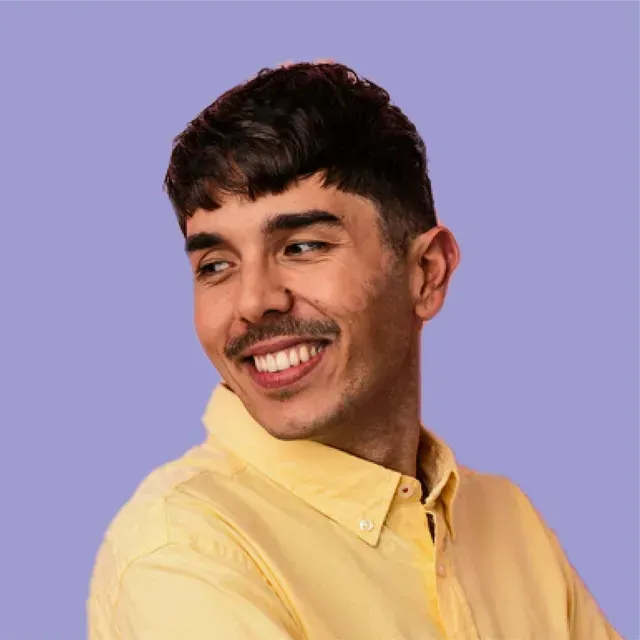 A man with a mustache is wearing a yellow shirt and smiling.
